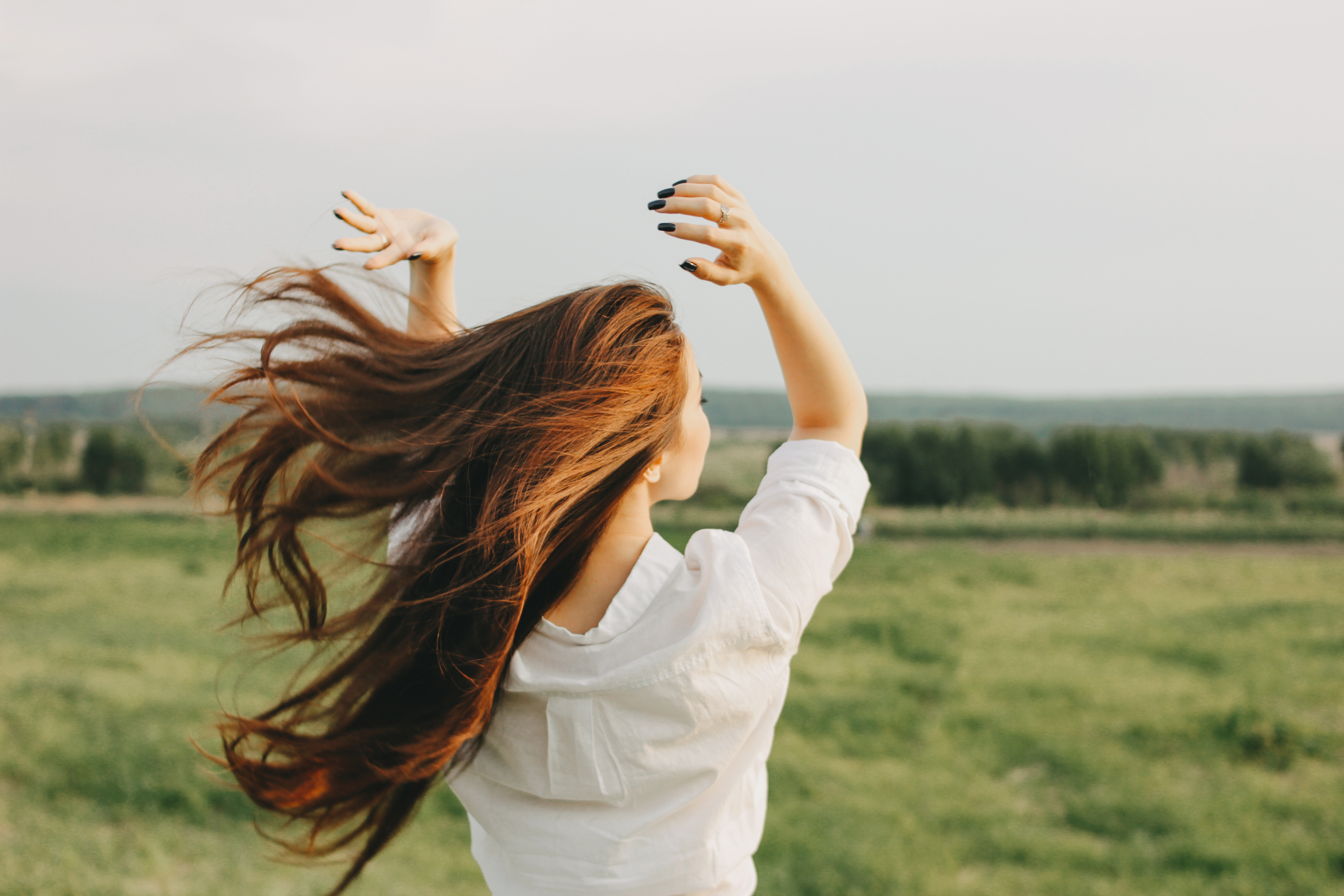 Stressabbau in der Natur. Frau mit langen Haaren, die im Wind fliegen, streckt die Hände in die Höhe.